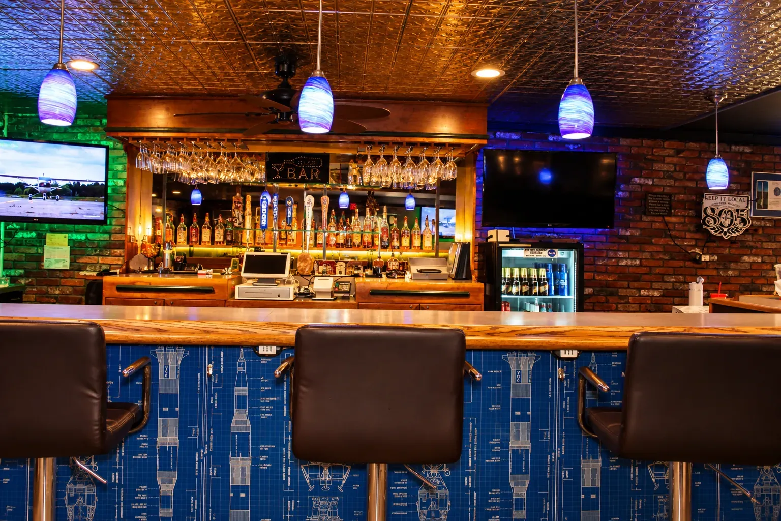 The bar at O'Cairns Bistro, with pendant lights, a tin ceiling and leather bar stools