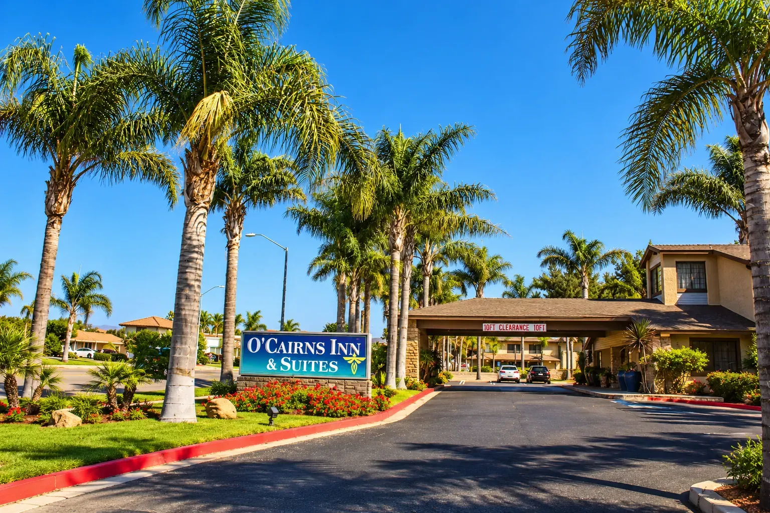 The front of O'Cairns Inn & Suites: the hotel sign, a palm-lined drive and the covered entrance