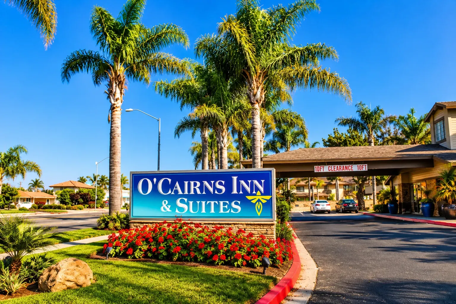 The O'Cairns Inn & Suites sign beside the entrance drive, framed by palm trees and red flowers