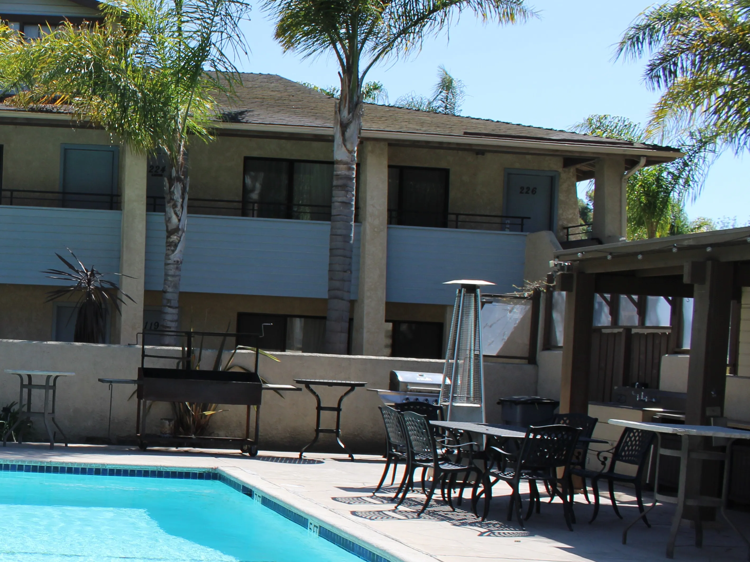 A Santa Maria-style grill cart and a gas grill on the pool deck, with a patio heater and a table and chairs for dining outside
