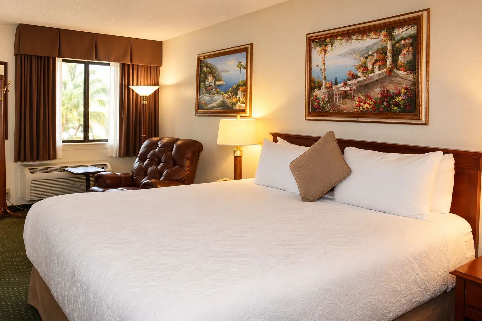 A guest room with one large bed, bedside lamps and a leather recliner by the window