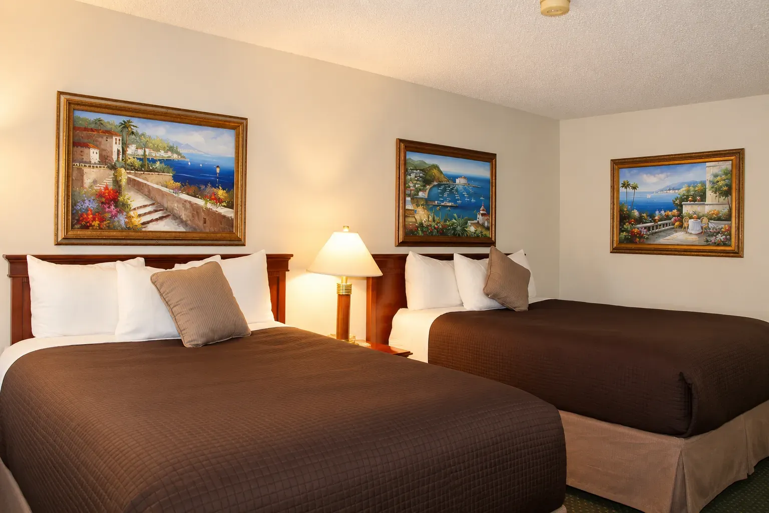 A guest room with two queen beds and framed paintings above them