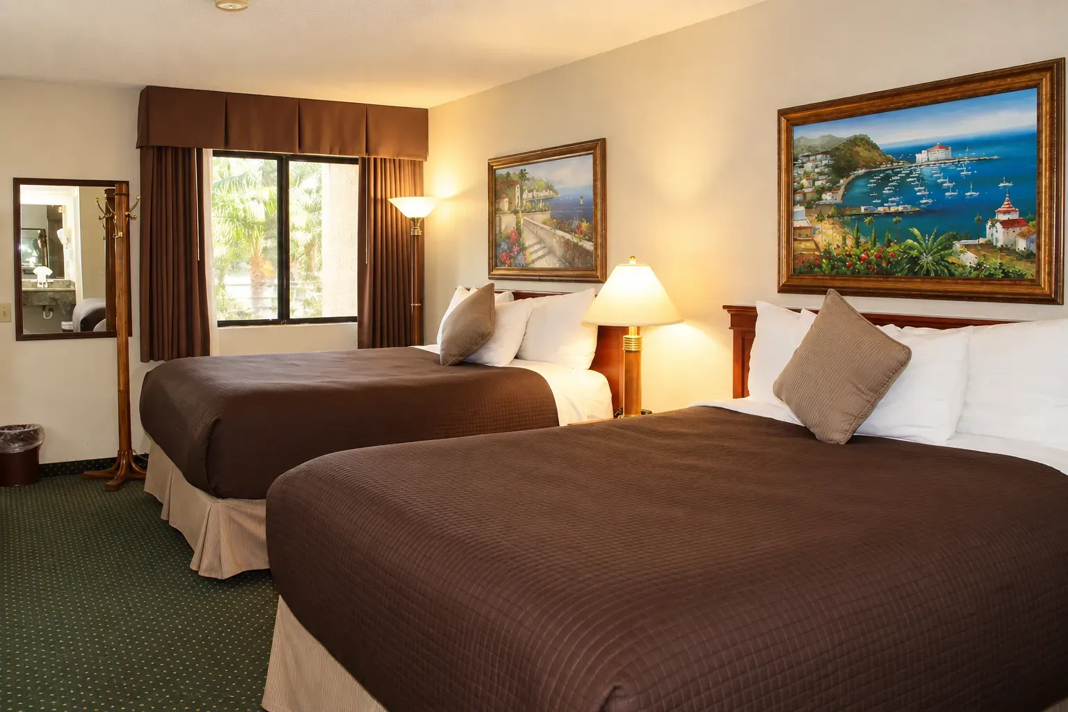 A guest room with two queen beds, seen from the entrance, with a window and a mirror